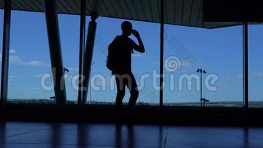 带着背包的年轻人站在机场休息室里打电话。